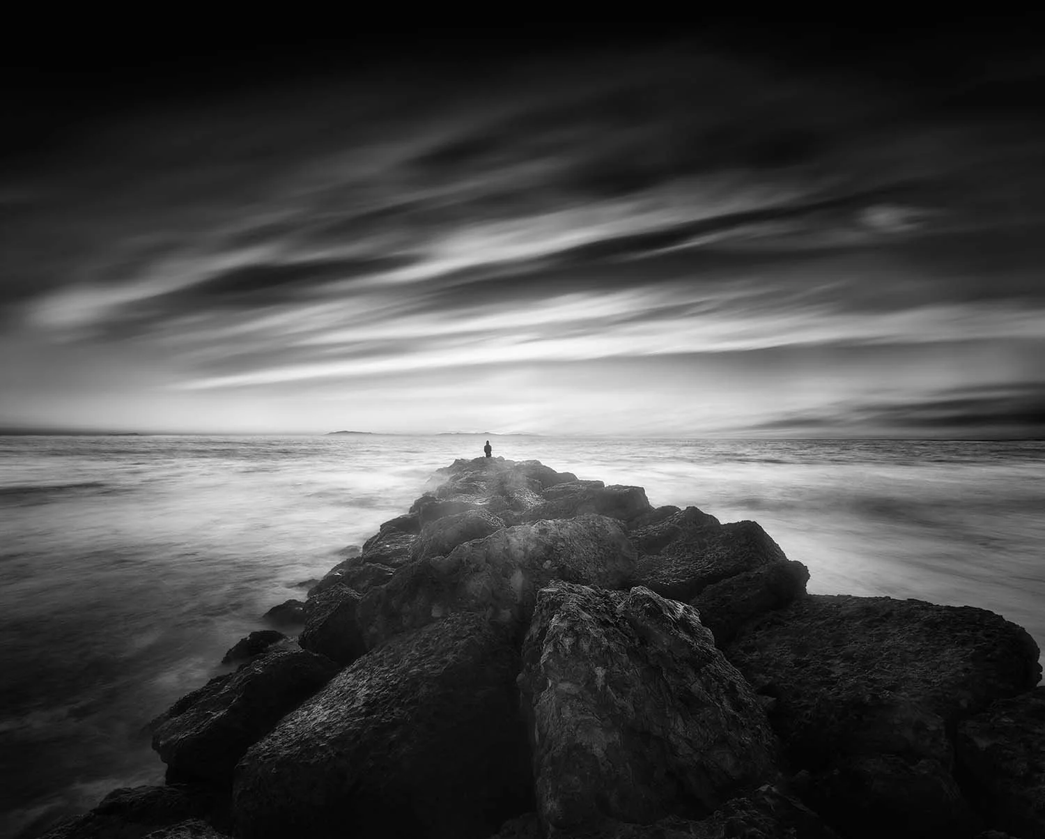 Lone figure on a rocky jetty under a dramatic sky